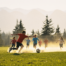 Children of many ethnic backgrounds playing soccer on a grassy field with snowy mountains in the distance